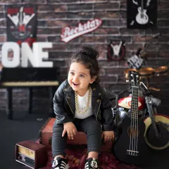 This little rockstar is ready for his first world tour! The leather jacket, gold chain, and guitar create a super cool vibe for a first birthday photoshoot.