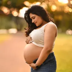 A close-up portrait bathed in warm, golden light. This outdoor shot focuses on the beautiful baby bump and the serene expression of the expecting mother.