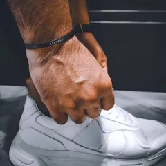 A man tying his shoelaces while wearing a black cuff bracelet engraved with 'AARUMANI'. This shows the bracelet as a durable accessory for an active, modern lifestyle.