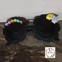 A close-up of the personalized kids' sunglasses. These flower-shaped frames are decorated with the name 'Naisha' in letter beads and other cute charms.