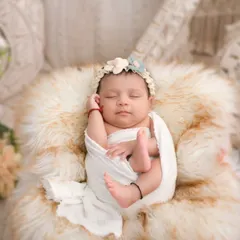 A peaceful newborn rests on a soft, cream-colored fur, adorned with a delicate floral headband. This photograph highlights our skill in posed newborn artistry, creating serene, beautiful portraits that focus on your baby's innocent features against a gentle, boho-inspired backdrop.