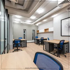 This co-working space is designed for flexibility and collaboration. The layout features individual desks with ergonomic blue chairs and an industrial aesthetic with exposed ceiling pipes, catering to a modern workforce.