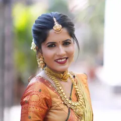 A radiant bridal portrait. The hairstyle is a traditional South Indian bun adorned with flowers, complementing her intricate gold jewelry and the rich colors of her muhurtham saree.
