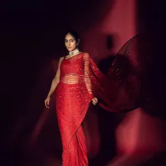 A dramatic fashion shot featuring a sleek, center-parted low bun. This hairstyle is modern and clean, allowing the striking red saree and the model's strong features to command attention.