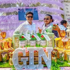 A happy guest and bartender pose behind the fully stocked gin bar. The setup features multiple bottles of Tanqueray gin, a large light-up 'GIN' sign, and an extensive selection of fresh garnishes for a vibrant party.