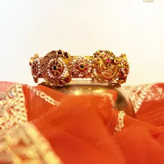 Gold that tells a story. This traditional bangle features three ornate medallions with delicate pearl borders and vibrant ruby centers. The vintage inspired craftsmanship makes this more than jewelry, it is wearable art.