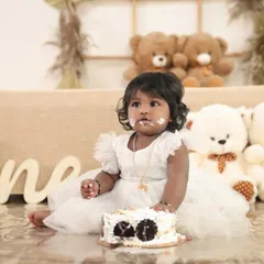 The aftermath of a successful cake smash! This little girl in a beautiful white dress is surrounded by teddy bears in this sweet and memorable first birthday photo.