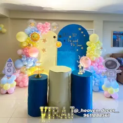 A "First Trip Around The Sun" space-themed birthday party. This cute setup features astronaut and rocket cutouts, a sun and stars backdrop, and a pastel-colored balloon garland.