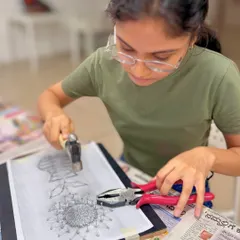 The first step in string art is carefully hammering nails along a printed template. This participant is focused on creating the outline for her sunflower design.
