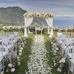 A breathtaking mountain view serves as the backdrop for this outdoor wedding ceremony. The aisle is scattered with white rose petals leading to a beautiful floral mandap, showcasing a romantic and natural theme.
