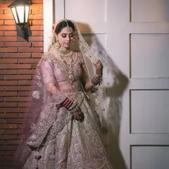 A full-length shot showing the bride in her magnificent lehenga. The soft lighting and elegant pose create a timeless portrait that feels like a painting.