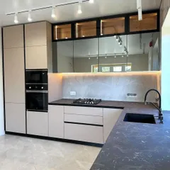 This kitchen design combines beige handleless cabinets with a dark countertop and mirrored backsplash. The mirror is a great way to make a smaller kitchen feel more spacious and bright.