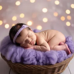 A classic newborn portrait, with the baby sleeping soundly in a basket on a soft purple wrap. The beautiful bokeh lights in the background add a touch of magic to this peaceful scene.