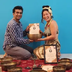 A joyful student receives her Sound Healing TTC certificate. The setup with multiple singing bowls highlights the immersive nature of this training.