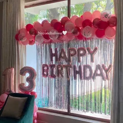 A pretty-in-pink theme for a 13th birthday. This home decoration features a silver fringe curtain, a garland of pink and red balloons, and large rose gold foil balloons for the number '13'.