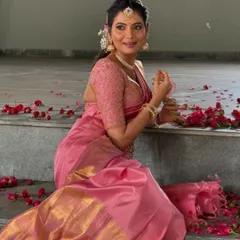 Shwetha Prasad seated amidst rose petals, looking lovely in the custom pink Kanchivaram saree and embroidered blouse.