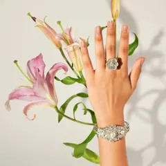 A model's hand, adorned with a floral-inspired ring and bracelet, is elegantly posed with fresh lilies. This image blends the beauty of nature with the intricate craftsmanship of fine jewellery.