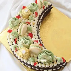 A beautiful crescent moon-shaped cake, perfect for Eid or Ramadan celebrations. This chocolate cake is decorated with green and white buttercream swirls, macarons, and Ferrero Rocher.