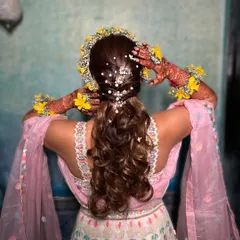 A view of the completed Haldi hairstyle from the back, adorned with a crown of yellow flowers and delicate pearls.