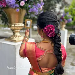 A back view of the bride's look, showing the intricate braid adorned with fresh flowers and the neat fall of the saree pallu. The gold vaddanam (waist belt) sits perfectly over the crisp pleats.
