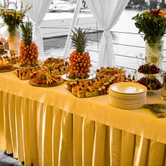 An elaborate fruit and appetizer buffet set up for an event by the water. The display features intricately carved pineapples and a colorful array of canapés, demonstrating our flair for creating visually stunning spreads.