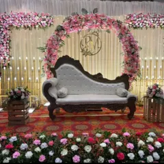A classic reception stage with a circular floral arch made of pink flowers. The decor includes a vintage-style chaise lounge for the couple and candle-lit props for a romantic glow.