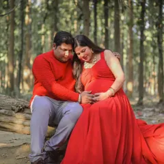 A quiet, intimate moment between expectant parents during their forest maternity shoot. The vibrant red of her dress contrasts beautifully with the natural surroundings.