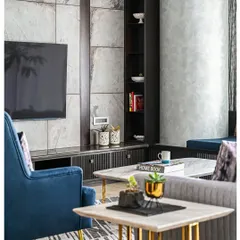 A closer view of the living area, highlighting the interplay of textures. The smooth, cool marble of the coffee tables contrasts with the soft velvet of the blue armchair and the textured grey paint on the structural column.