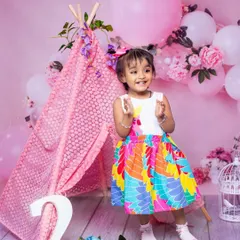 A joyful toddler claps her hands with excitement during her second birthday photoshoot. The colorful dress and pink teepee setup make this a vibrant and happy celebration.