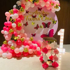 This is a popular butterfly theme decoration I did for a first birthday. It features a dense balloon arch in shades of pink and white, accented with gold and pink butterflies, and a large light-up marquee number '1'.