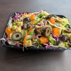 A takeaway container filled with a colorful mix of fresh vegetables, including carrots, cabbage, and olives. This is the base we use for many of our salads, ensuring every bite is crisp and nutritious.