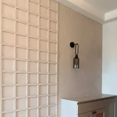 A bohemian-inspired foyer unit with a textured wall panel featuring square woodwork. The design is complemented by a sleek black wall sconce, mixing earthy textures with modern accents.
