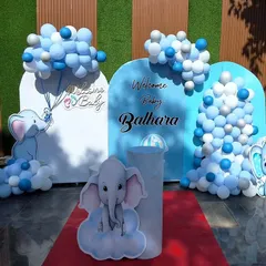 An adorable elephant-themed 'Welcome Baby' decoration. This outdoor setup uses multiple backdrops, cute elephant cutouts, and blue and white balloon clouds to create a whimsical scene.
