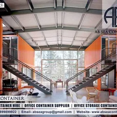 The interior of this multi-level container home reveals a spacious, open-plan design with a double-height ceiling and dramatic staircases. The original orange container walls are left exposed for an industrial-luxe feel.