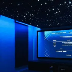 We create more than just a technical setup; we build an atmosphere. This room features integrated blue ambient lighting and a fiber-optic starfield ceiling, which work in concert with the Dolby Atmos sound system to create a truly immersive and luxurious environment for any viewing or listening session.