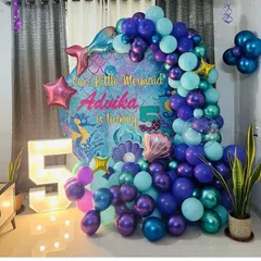 An enchanting "Our Little Mermaid" theme for a 5th birthday. This setup features a deep-sea-inspired balloon arch in shades of purple and teal, a custom backdrop, and a large light-up number '5' to make a splash.
