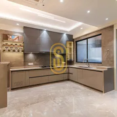 A complete view of a sleek, modern modular kitchen. This L-shaped layout maximizes space and functionality, featuring dual-tone cabinets, a built-in hob, and under-cabinet lighting for a bright and efficient cooking environment.