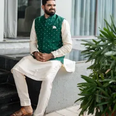 A great example of styling for a pre-wedding event. The groom looks dapper and relaxed in an off-white kurta paired with a stylish green mirror-work Nehru jacket, ready for his engagement ceremony.