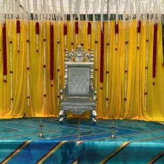 A closer look at the majestic throne and vibrant backdrop for an outdoor ceremony. This view highlights the intricate details of the silver chair and the rich texture of the yellow drapes.