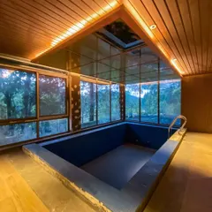 An evening view of the indoor pool area under construction. The warm interior lighting contrasts beautifully with the twilight sky, showcasing the space as a year-round retreat.
