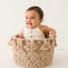 Peeking out with a happy grin. The same baby boy gives a different, adorable expression from his cozy basket during his milestone photoshoot.