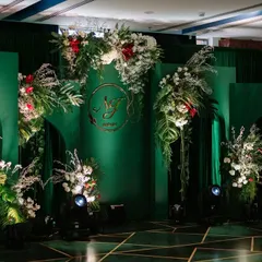 A stunning stage backdrop for a reception or engagement. I used emerald green panels with modern arches, adorned with lush arrangements of white flowers and tropical green leaves. The couple's monogram in gold adds a personalized, elegant touch.