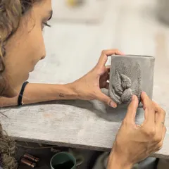 A student carefully adds a textured leaf appliqué to her hand-built mug. This surface decoration technique allows for intricate and personal designs.