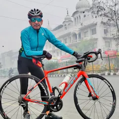A member with his bright orange Giant Defy bike in front of a Gurudwara, blending cycling with city culture.