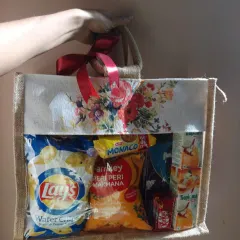 A wedding snack hamper designed as a welcome gift for guests. This floral jute bag with a clear window contains chips, biscuits, and juices to provide a refreshing treat.