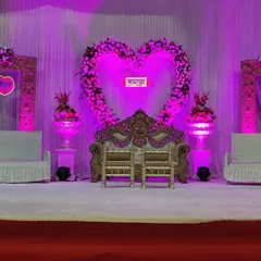 A romantic engagement stage featuring a large heart-shaped floral arch as the centerpiece. The entire setup is bathed in a soft purple light, creating a dreamy atmosphere for the couple's special moment.