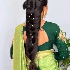 A stunning and intricate long braid, adorned with a stylish bow made from hair and scattered pearls. This is a trending hairstyle for modern brides.