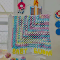 This pastel granny square blanket, customized with "Baby Gunnu," is a classic choice. The addition of multi-colored pom-poms on the corners makes it extra special and fun for a little one.