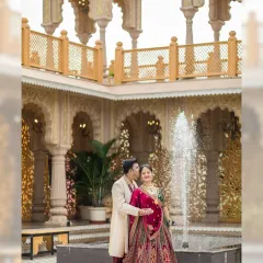 A romantic moment by a courtyard fountain, with beautiful palace architecture in the background. The groom whispers to his bride, creating a candid and sweet memory.