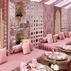 A closer look at the intricate details of a pink-themed reception. The seating arrangement features beautiful mirrored jaali work, plush pink cushions, and traditional silver serveware, blending classic charm with a modern color palette.
